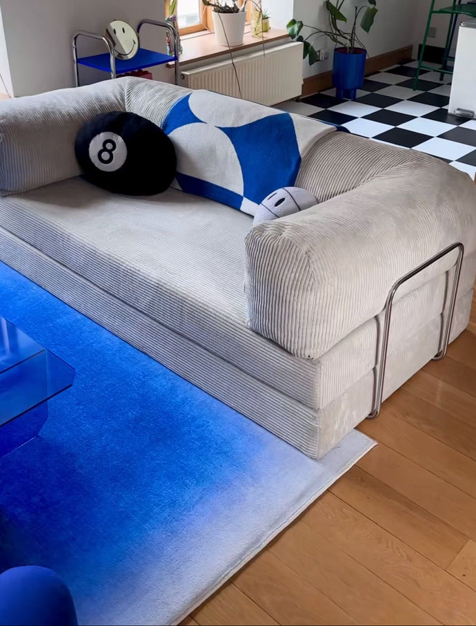 Beige sofa with decorative pillows in a room with a checkered floor and plants.